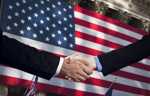 People shake hands and make an agreement in front of the American flag