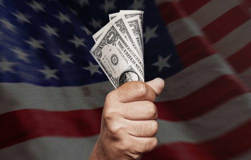 Unrecognizable young man holding US Dollar over American flag.