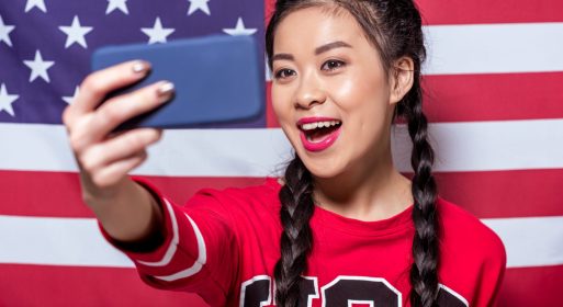 portrait of smiling woman taking selfie on smartphone with american flag behind